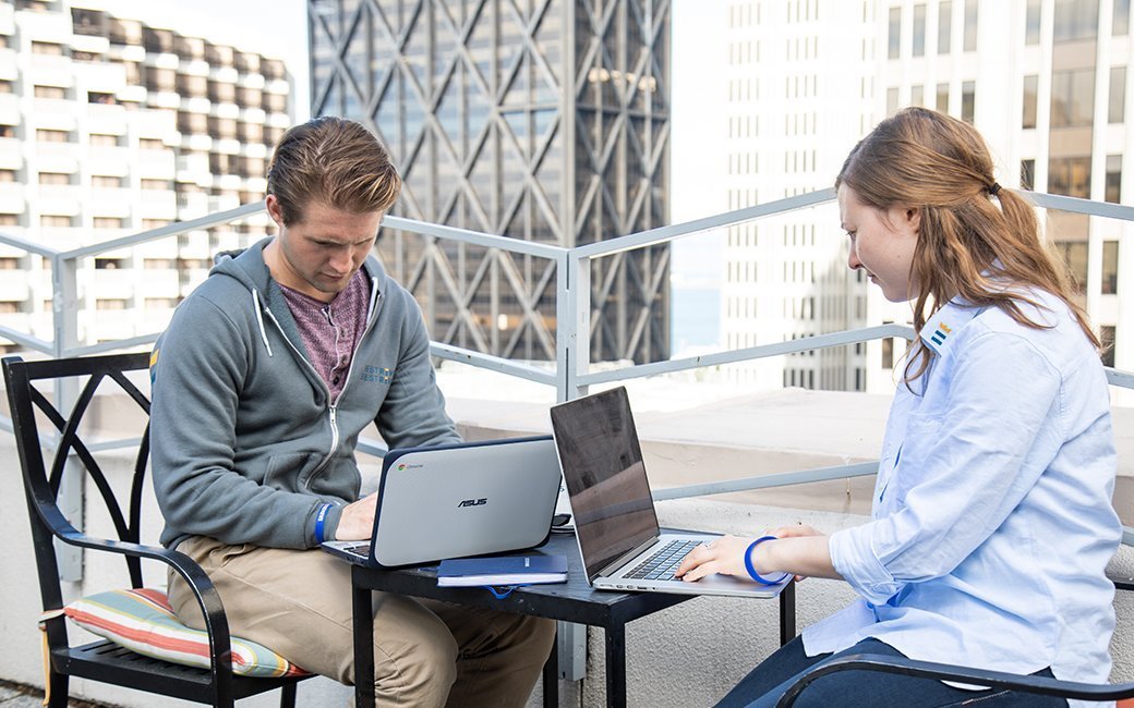 Two people sitting outside at a table on ultrabooks