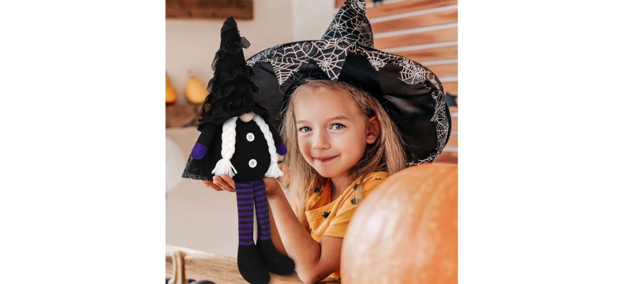 Little girl in witch's hat holding plush Halloween gnome
