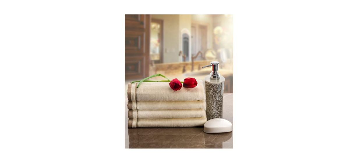 A set of 4 beige and brown towels with embroidered trim witting on a counter by soap and some roses
